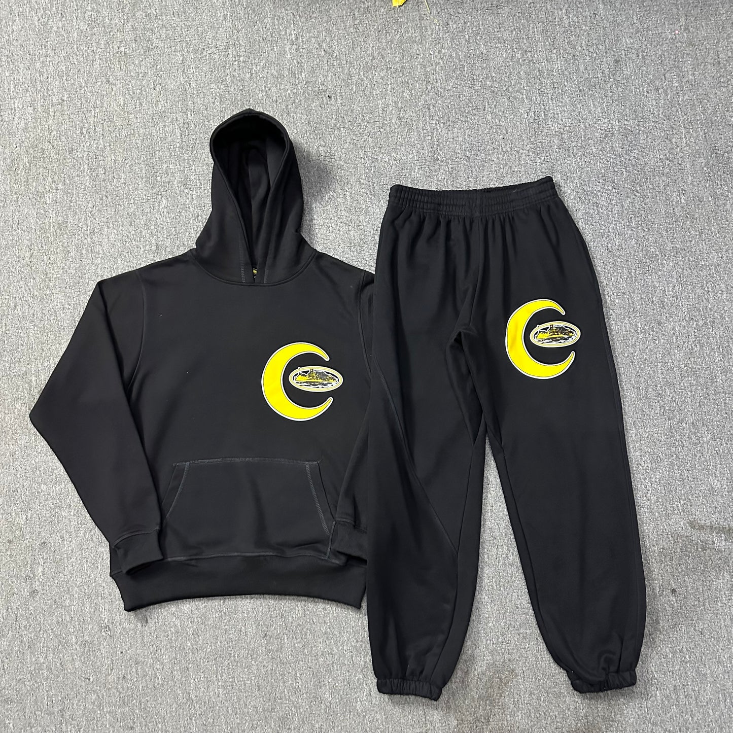Black hoodie and pants set with yellow logo on a gray background